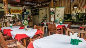 A restaurant with wooden tables and chairs, red tablecloths, and a green napkin holder. - Klong Muang Inn (Krabi)
