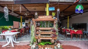 An outdoor dining area with tables and chairs, a wooden decorative structure, and hanging lights. - Klong Muang Inn (Krabi)