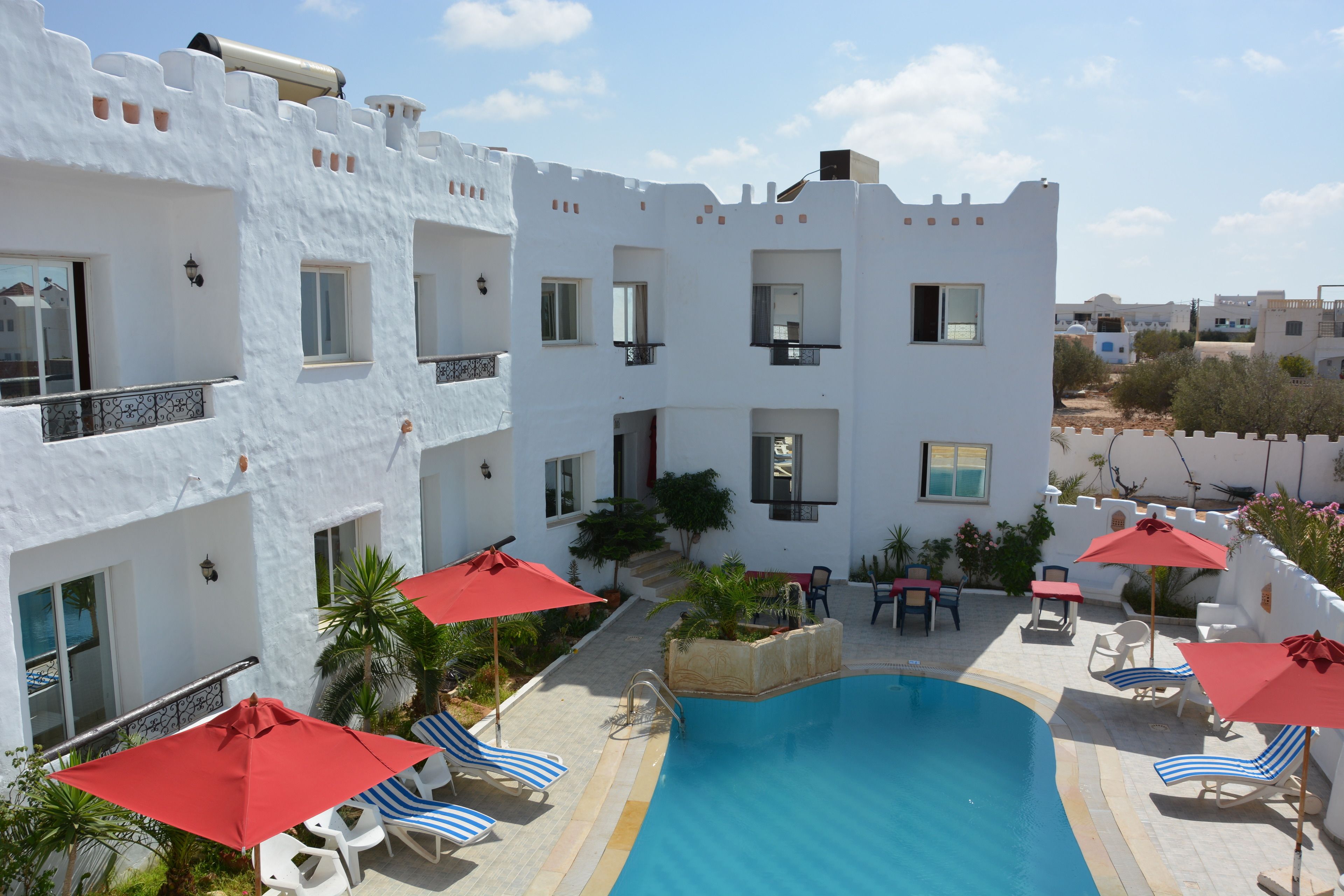 Un bâtiment blanc doté de balcons, d’une piscine et de parasols rouges.