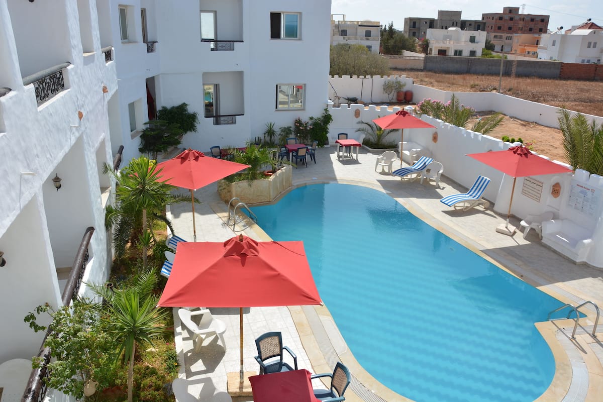 A pool area with lounge chairs and umbrellas, surrounded by white buildings with balconies.