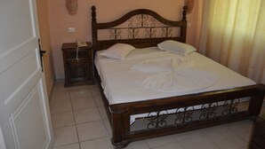 Een slaapkamer met een houten bed, witte lakens, een nachtkastje met een telefoon en een wandlamp.