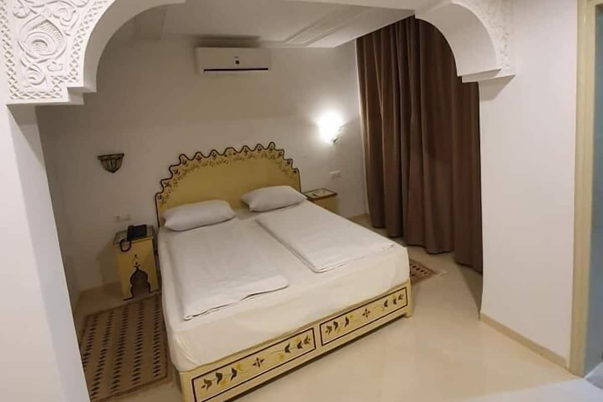 A bedroom with a bed, a nightstand, a wall-mounted lamp, and a window with curtains.