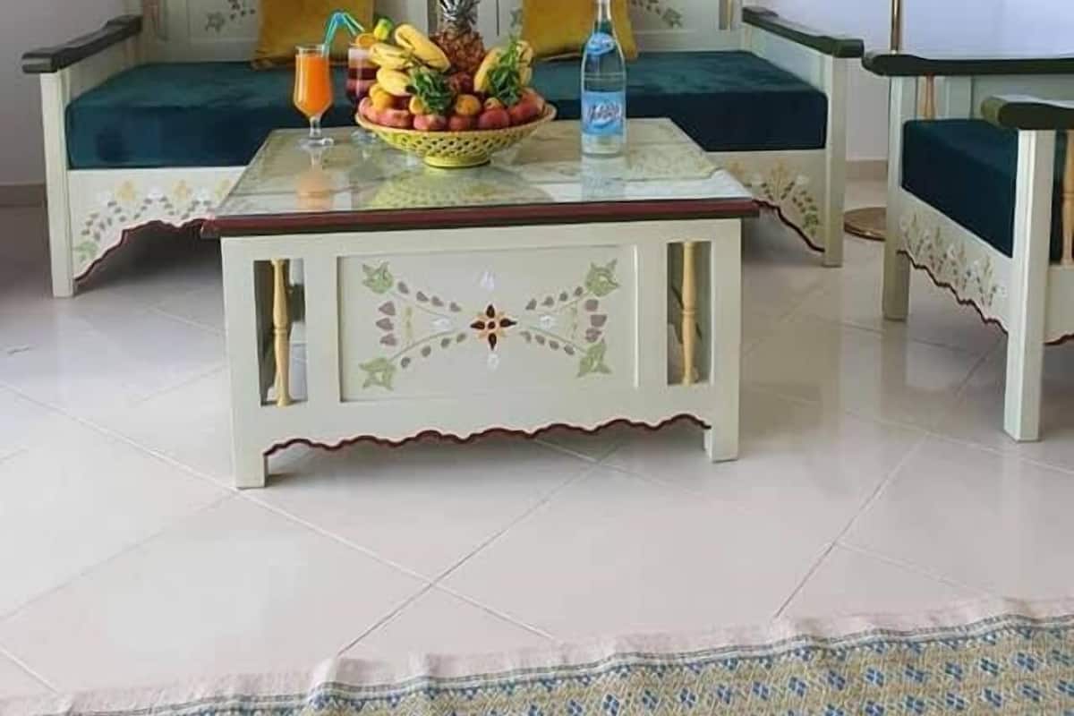 A room with a sofa, a coffee table with fruit and a drink, a lamp, and a painting on the wall.