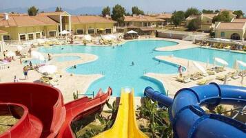 Relax by the pool with lounge chairs and umbrellas, surrounded by Mediterranean-style buildings and water play options.