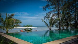 Una piscina infinita de agua cristalina, rodeada de vegetación tropical y con vistas a una playa que incluye una pequeña isla.