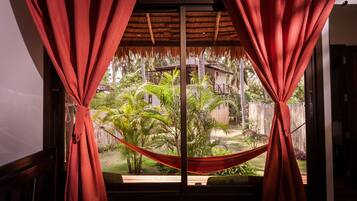 Una habitación con vista a un jardín a través de una ventana con cortinas rojas atadas.