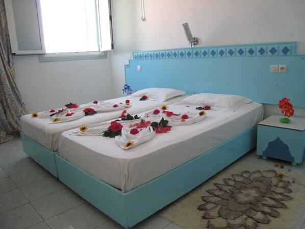 A bed with white linens and red flowers, a blue headboard, a nightstand with a vase, and a patterned rug. - Houria House Sable d'Or (Mahdia)