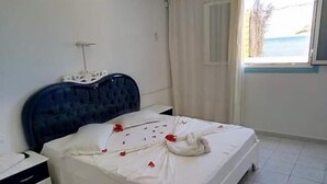 A bedroom with a bed, a nightstand, a window with curtains, and a view of the outdoors. - Houria House Sable d'Or (Mahdia)