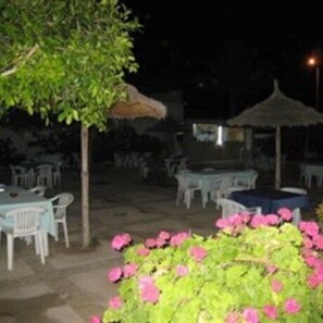 An outdoor seating area with tables and chairs, surrounded by greenery and a decorative flower arrangement. - Houria House Sable d'Or (Mahdia)
