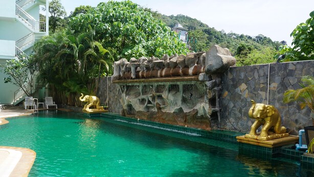 Una piscina con dos estatuas doradas de elefantes, rodeada por un muro de piedra y abundante vegetación.