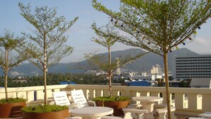Terraza en la azotea con mobiliario exterior, plantas en macetas y vistas a un paisaje urbano y montañas.