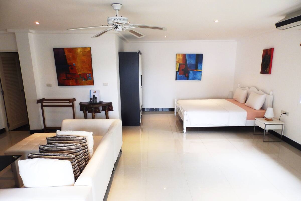 A modern hotel room with a bed, a sofa, a small table, and artwork on the walls.