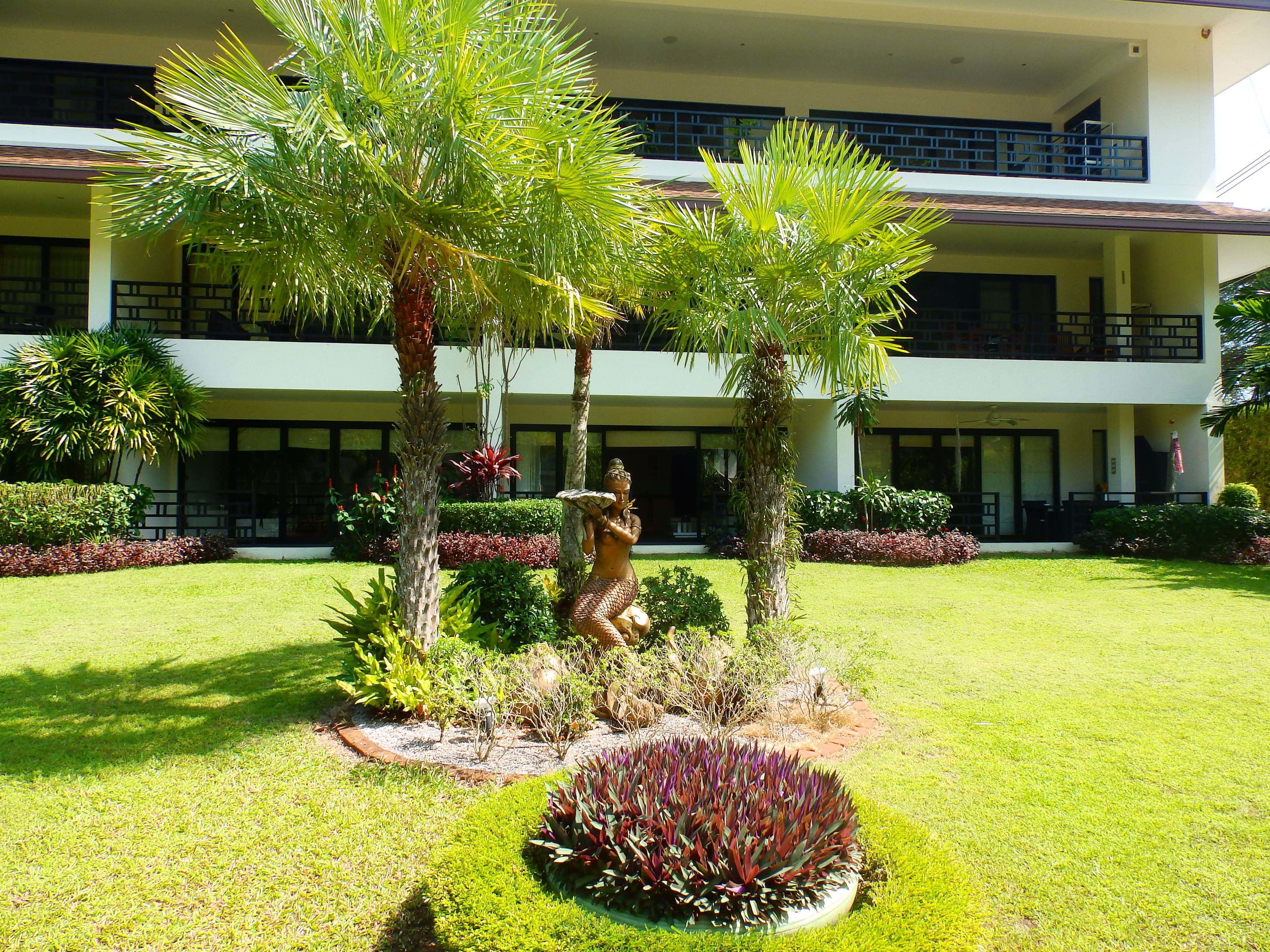 A courtyard with palm trees, a statue, and a building with balconies.