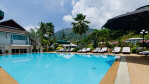 A swimming pool with lounge chairs and umbrellas, surrounded by palm trees and buildings. - Serenity Lakeside Resort (Kathu)