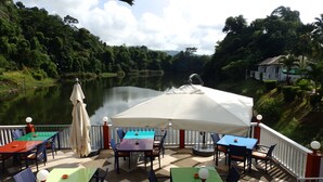 An outdoor dining area with tables and chairs, overlooking a lake. - Serenity Lakeside Resort (Kathu)
