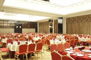 Un salón de banquetes con filas de mesas y sillas, techos altos y paneles decorativos en las paredes.