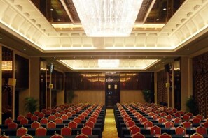Un salón de conferencias con filas de sillas, una araña de cristal y suelo alfombrado.