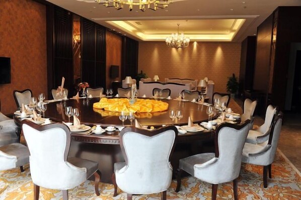 Una mesa redonda de comedor con varias sillas, una araña y piso alfombrado.