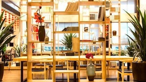 Una biblioteca con estanterías de madera, una mesa central y plantas en macetas.