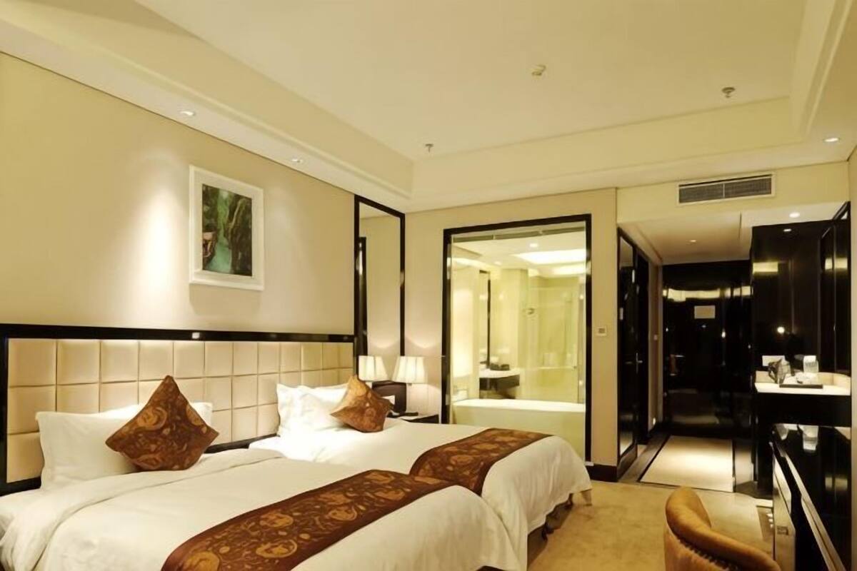 Quarto de hotel com duas camas, um espelho grande, banheiro e televisão.