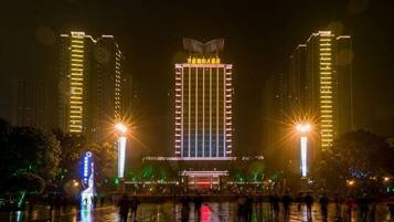 Un edificio de varios pisos con una entrada central, rodeado por una plaza húmeda que refleja luces.