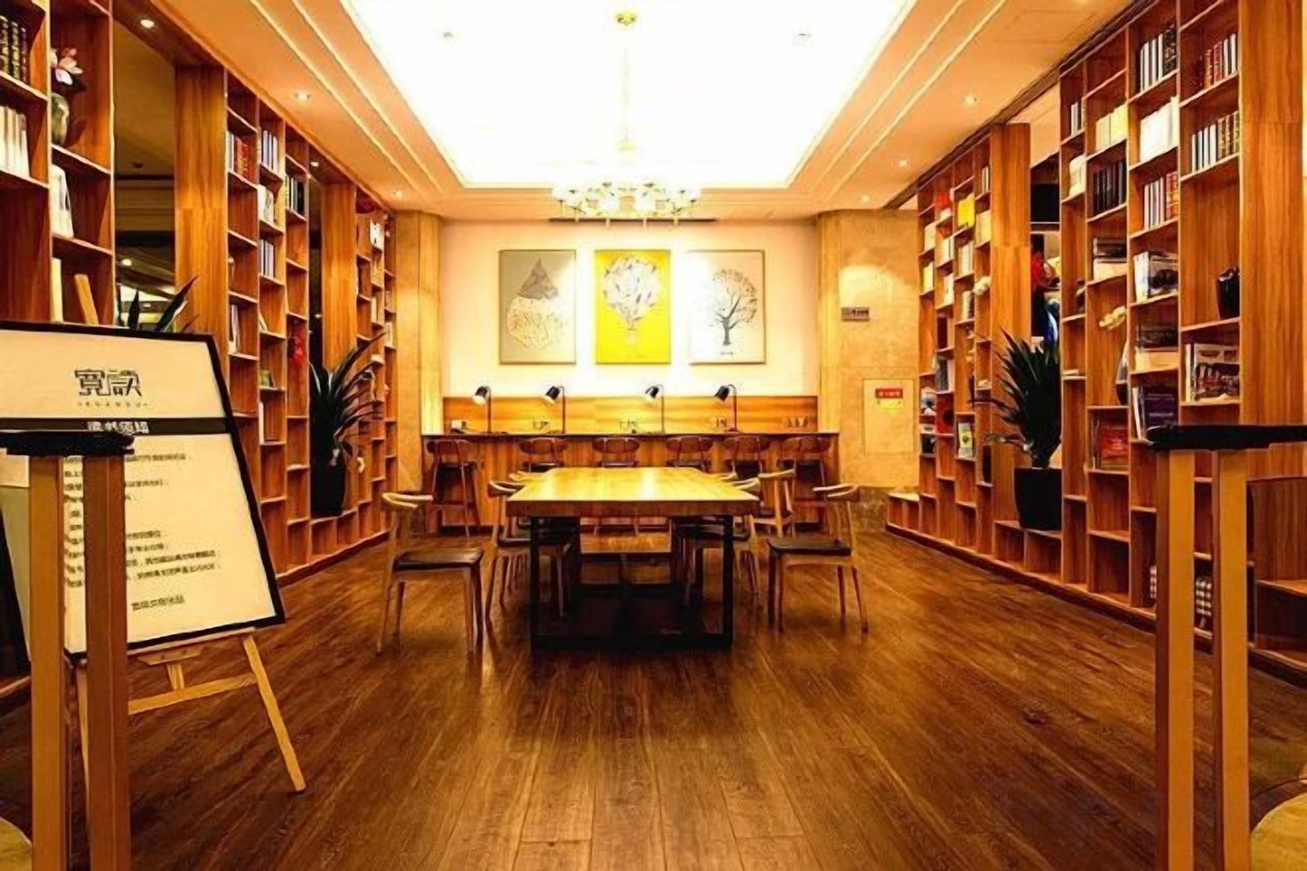 A library with wooden bookshelves, a central table, and a chandelier.