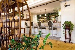 A bar area with a wooden bookshelf, white bar stools, and a plant on a stand. - Wansheng International Hotel (Chongqing)