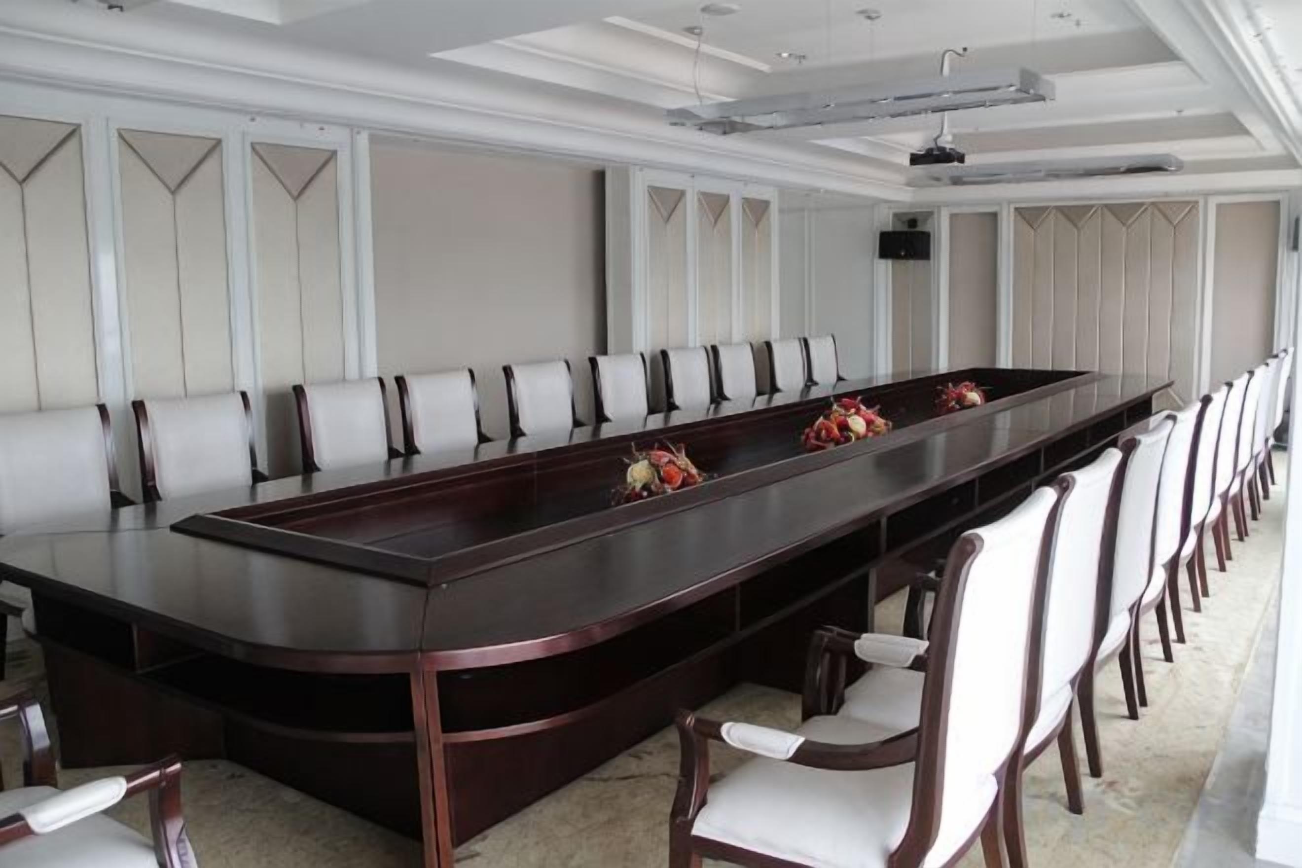 Un salón de conferencias con una larga mesa, sillas, un proyector y un orador.
