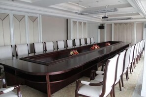 Un salón de conferencias con una larga mesa, sillas, un proyector y un orador.