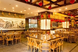 Un interior de restaurante con varias mesas y sillas, un mural en la pared y faroles rojos tradicionales.