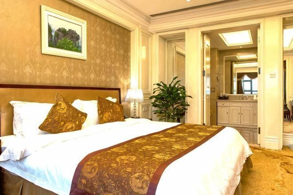 Quarto de hotel com uma cama grande, uma mesinha de cabeceira, um espelho e um vaso de planta.