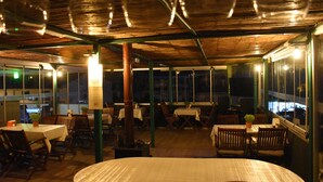 Um espaço de refeições interno com mesas e cadeiras, teto de madeira e grandes janelas.