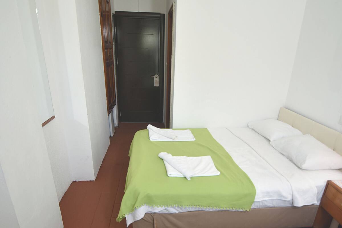 Habitación de hotel con dos camas, cada una con colcha verde y ropa blanca, y una puerta de madera al fondo.