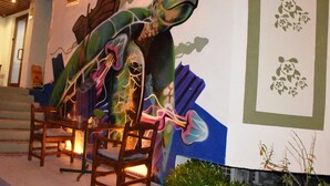 Um mural com um dinossauro numa parede, cadeiras de madeira e uma escada.