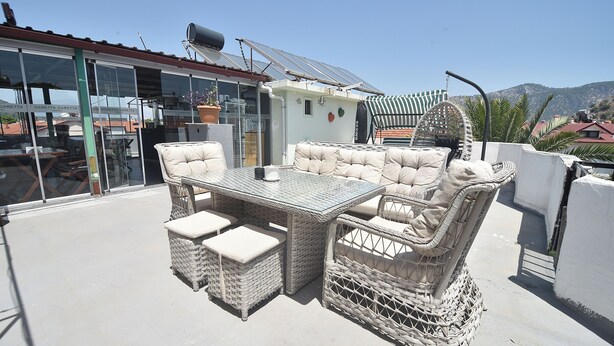 Um terraço no telhado com móveis de vime, uma porta de vidro e painéis solares.
