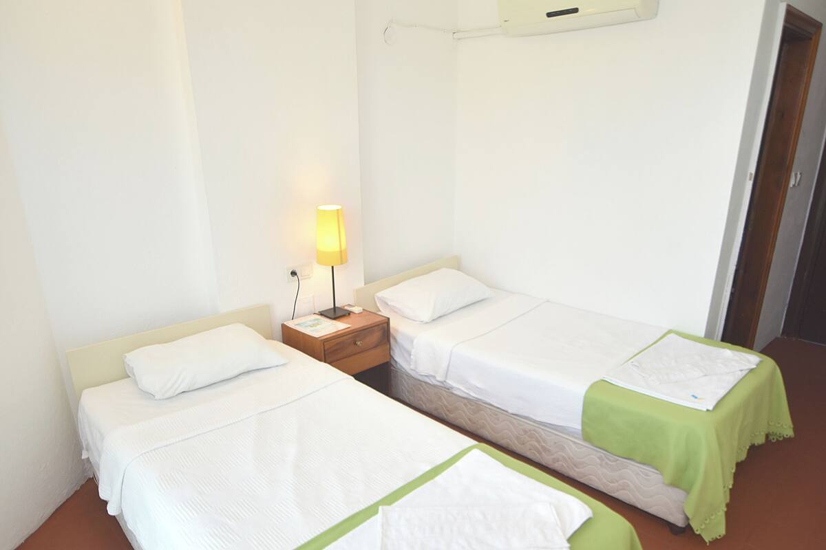 Habitación de hotel con dos camas individuales, una mesita de noche con lámpara y aire acondicionado instalado en la pared.