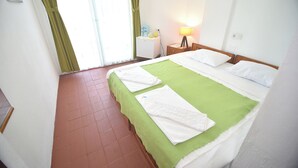 Quarto de hotel com cama, mesa de cabeceira, abajur e janela com cortinas.
