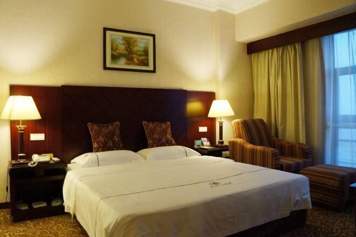 Een hotelkamer met een groot bed, twee nachtkastjes met lampen, een stoel, een raam met gordijnen en een schilderij aan de muur.