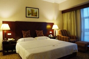 Una habitación de hotel con una cama grande, dos mesitas de noche con lámparas, una silla, una ventana con cortinas y un cuadro en la pared.