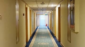Un pasillo de hotel con piso alfombrado, puertas a ambos lados y una fuente de luz al final.