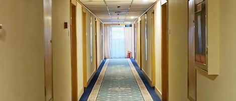 A hotel hallway with a carpeted floor, doors on both sides, and a light source at the end.