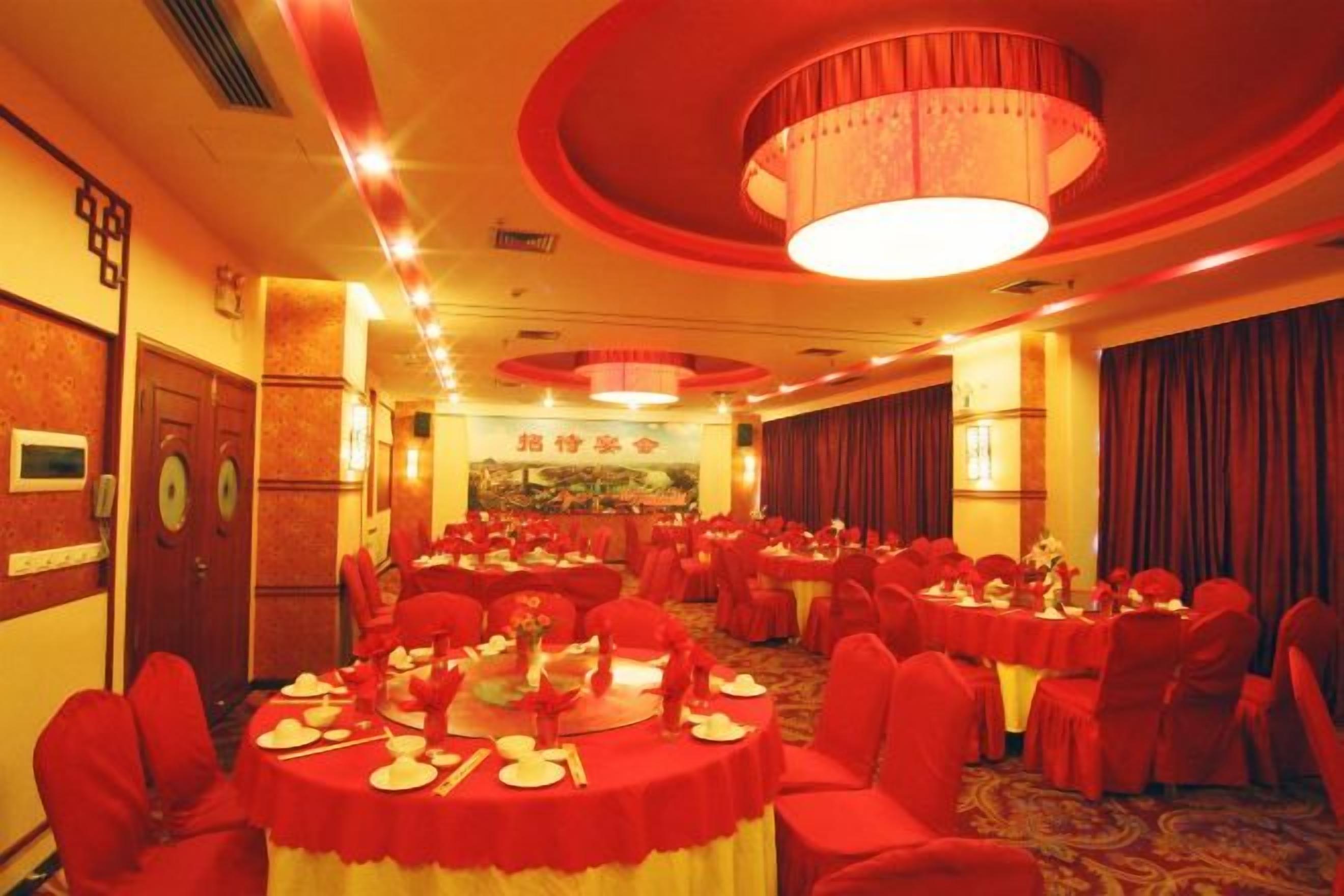 Un salón de banquetes con mesas redondas, sillas rojas y una lámpara de araña.