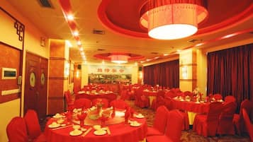 Un salón de banquetes con mesas redondas, sillas rojas y una lámpara de araña.