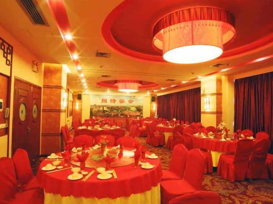 A banquet hall with round tables, red chairs, and a chandelier.