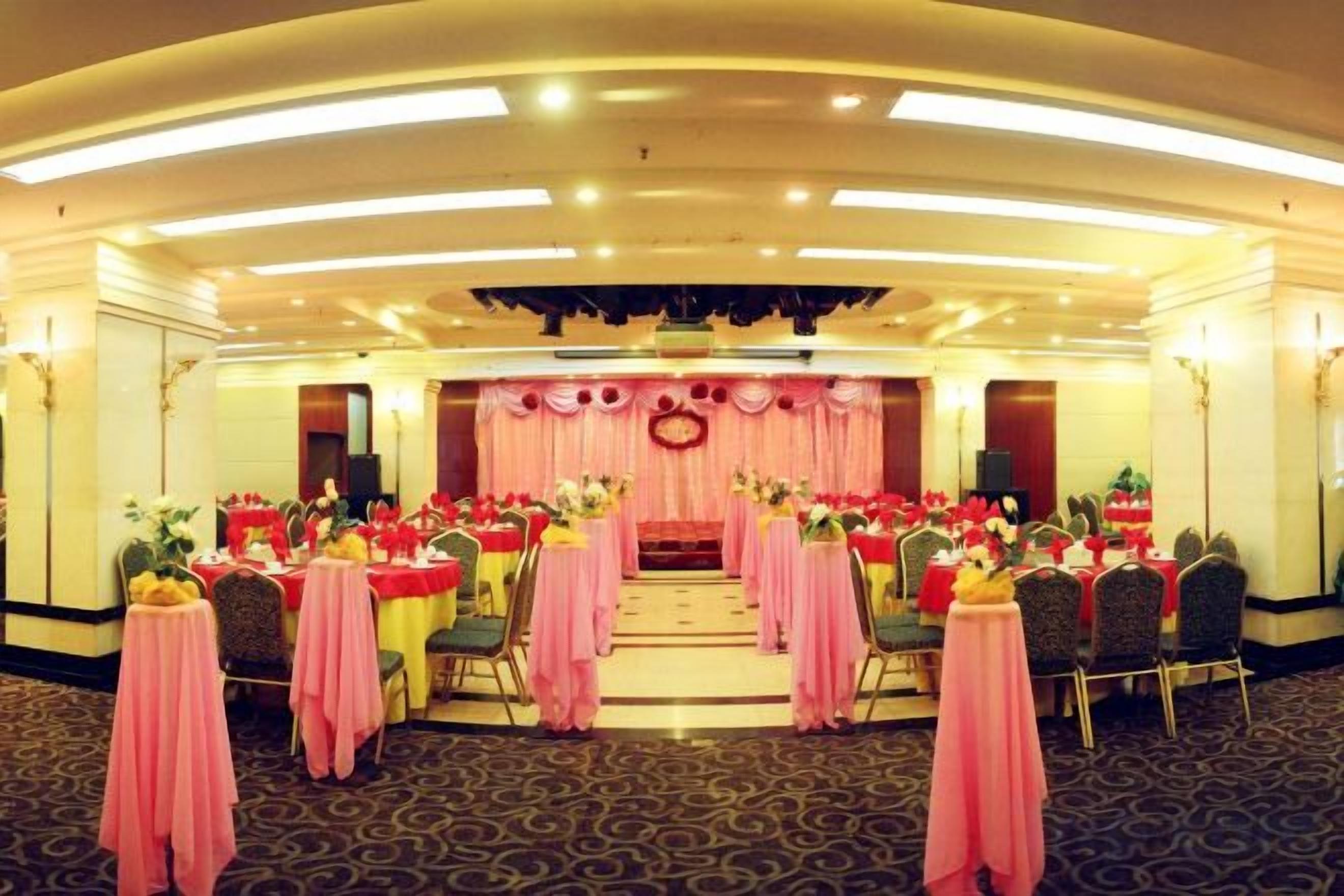 Uma sala de banquetes com mesas redondas, cadeiras e um palco com arranjo floral.
