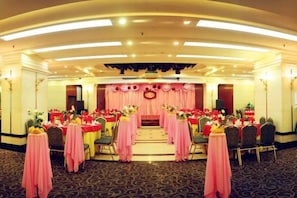 A banquet hall with round tables, chairs, and a stage with a floral arrangement. - Yan'an Grand Hotel (Liuzhou)