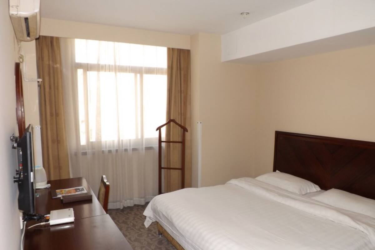 A hotel room with a bed, a desk, a chair, a TV, and a window with curtains.