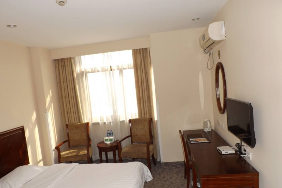 A hotel room with a bed, two chairs, a small table, a desk with a computer, and a TV.