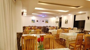 Uma área de refeições com várias mesas e cadeiras, algumas com centros de mesa florais.