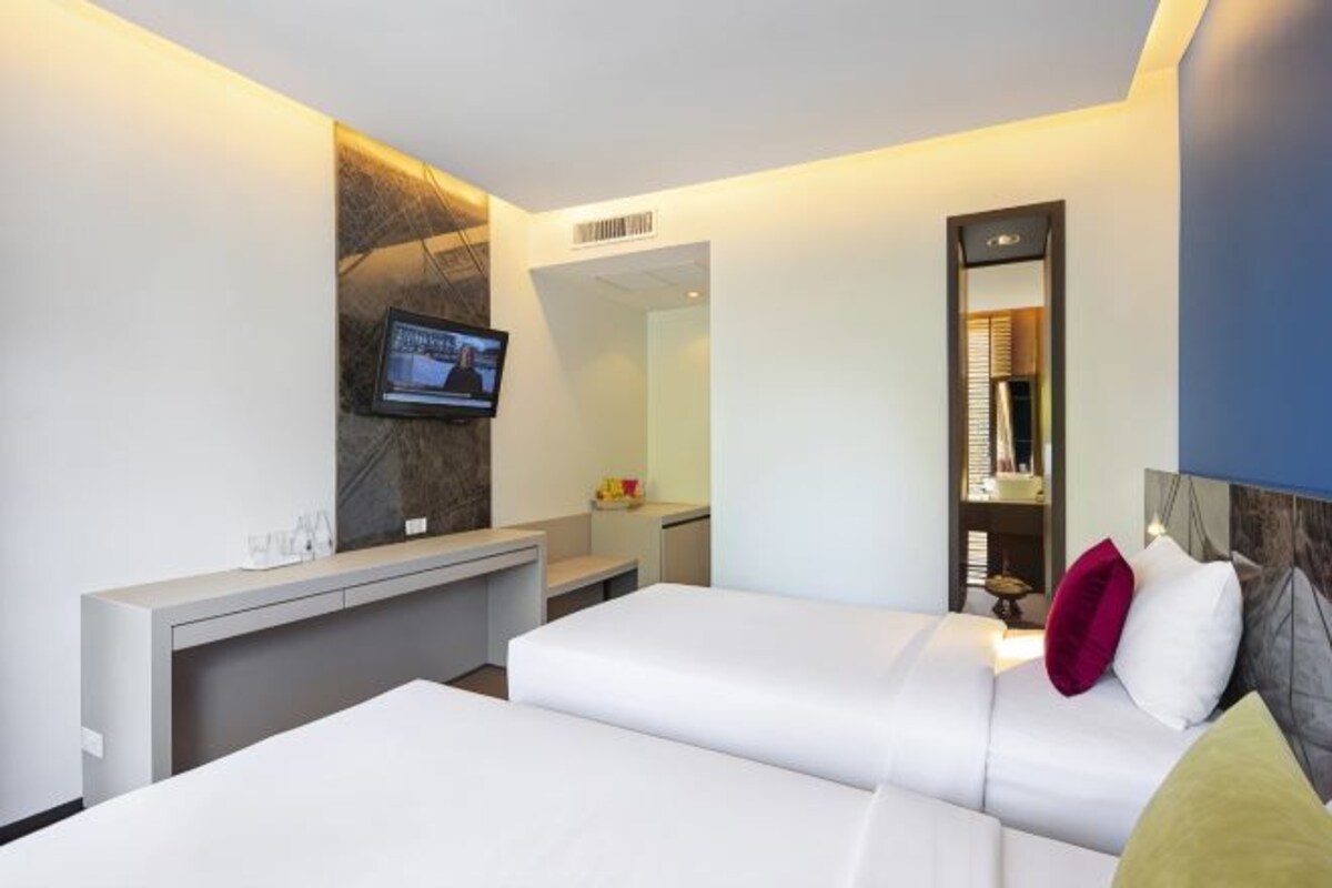A modern hotel room with a large bed, a desk, a television mounted on the wall, and a mirror.